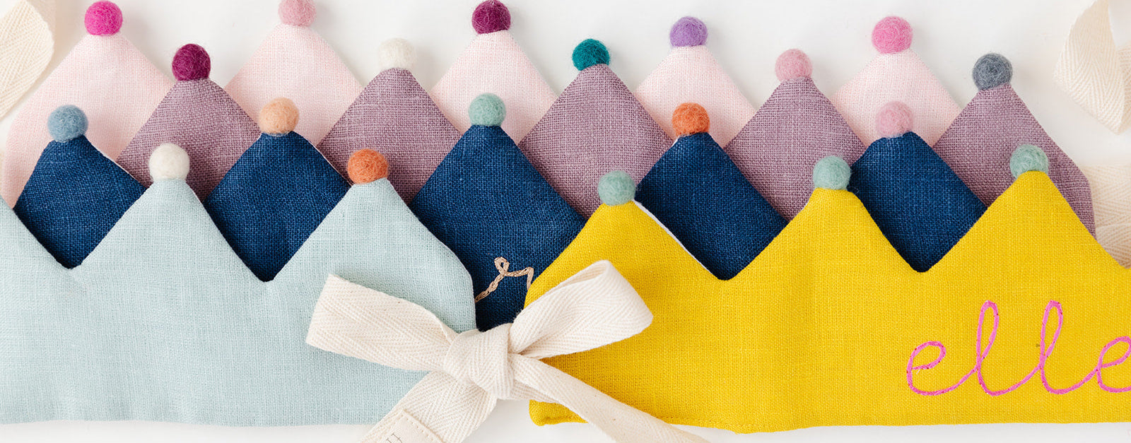 Colorful fabric crowns with pom-poms and a yellow banner with 'elle' on a white background