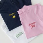Navy, pink, and white shirts with embroidered names on a light gray background