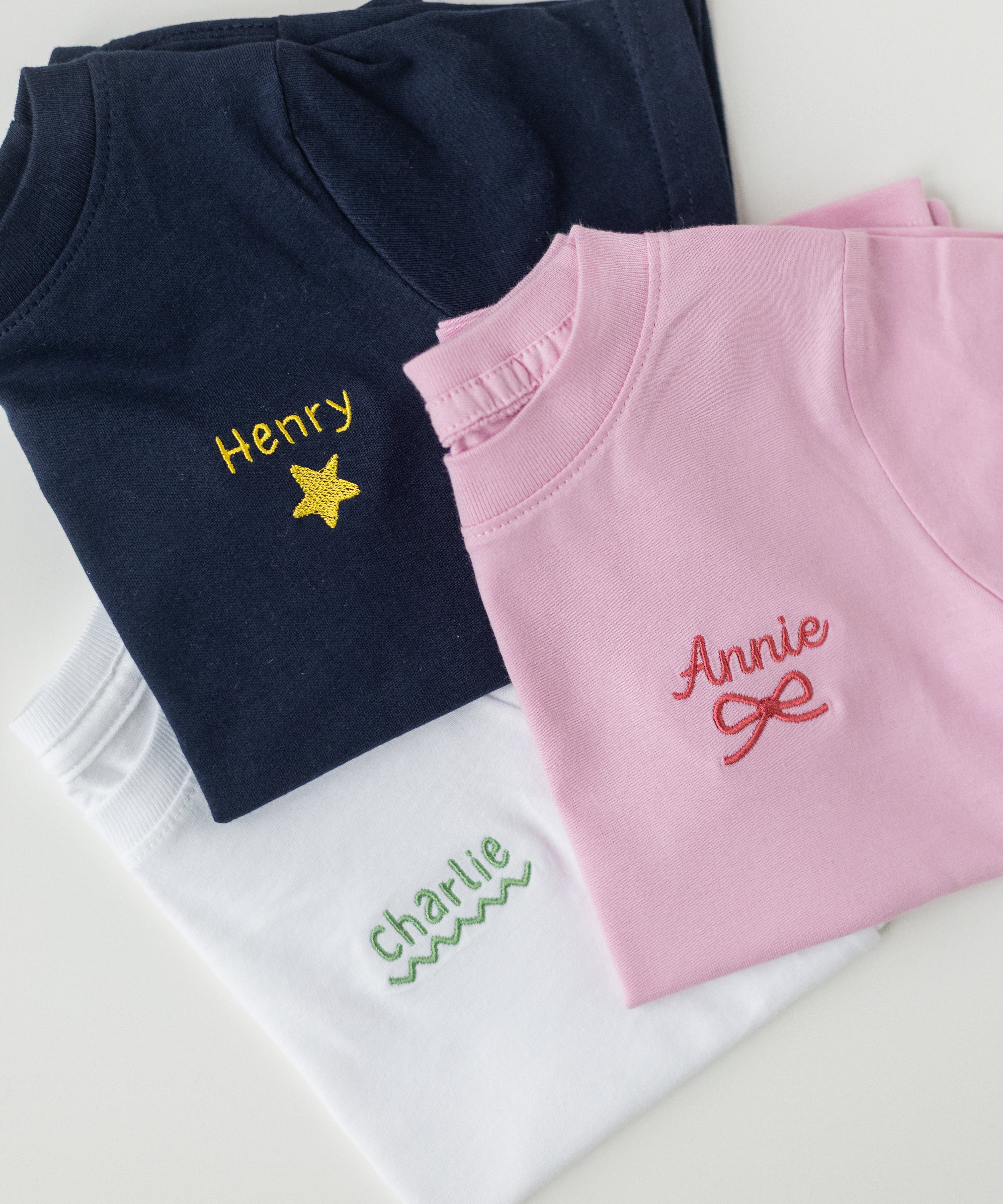 Navy, pink, and white shirts with embroidered names on a light gray background
