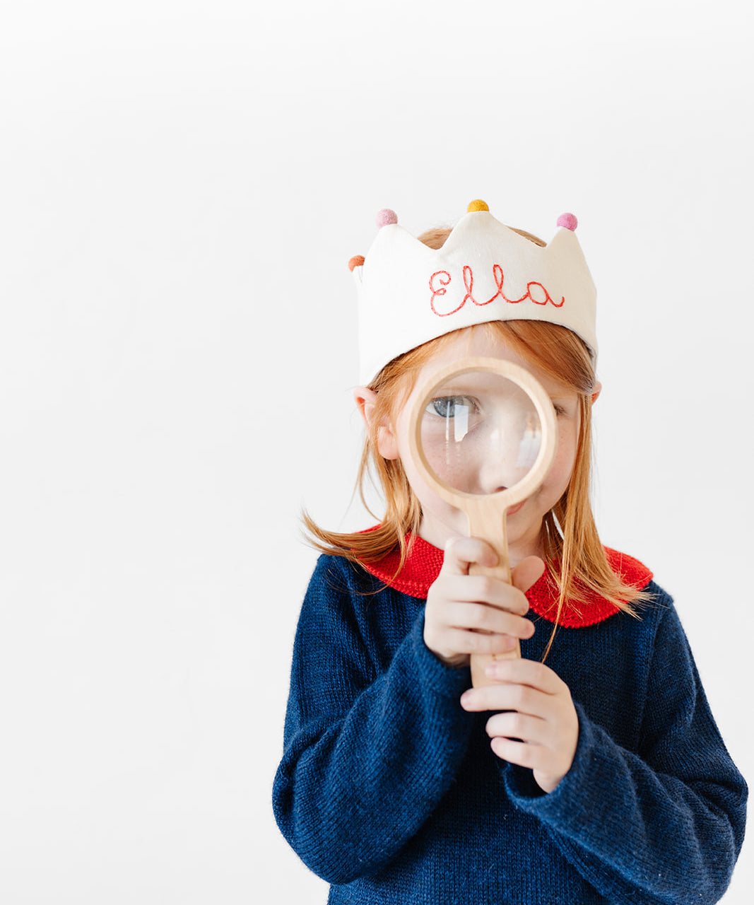 Girl wearing custom crown with name stitched holding a magnifying glass