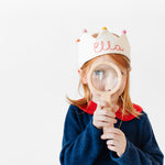 Girl wearing custom crown with name stitched holding a magnifying glass