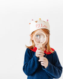 Girl wearing custom crown with name stitched holding a magnifying glass
