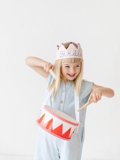 girl wearing pink birthday crown and playing drum
